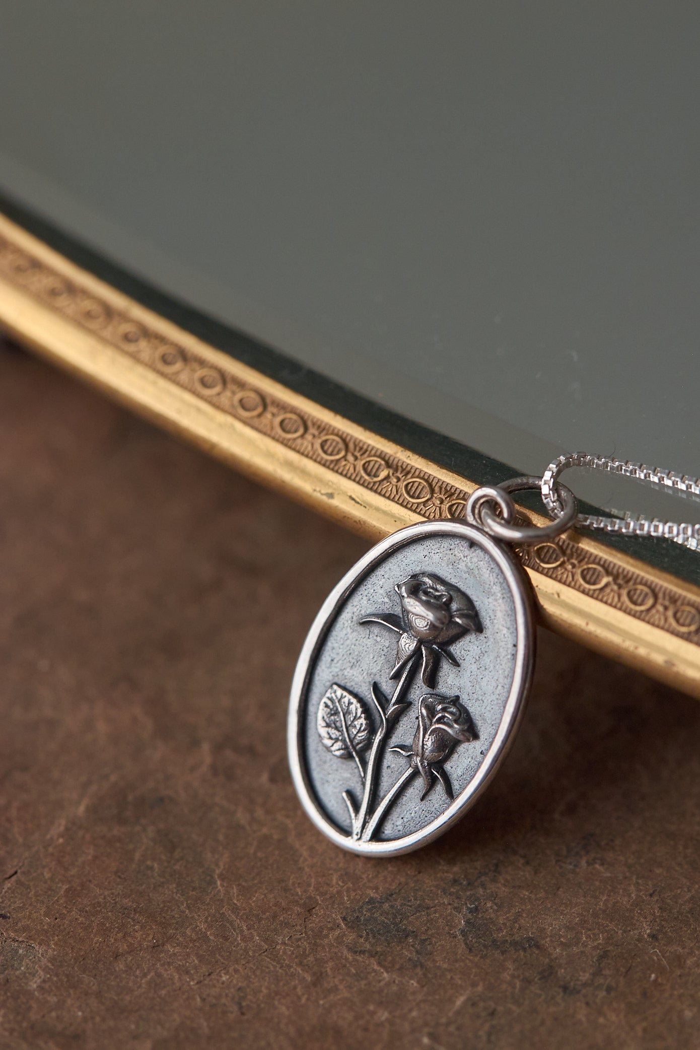 Silver pendant with rose design on a dark surface