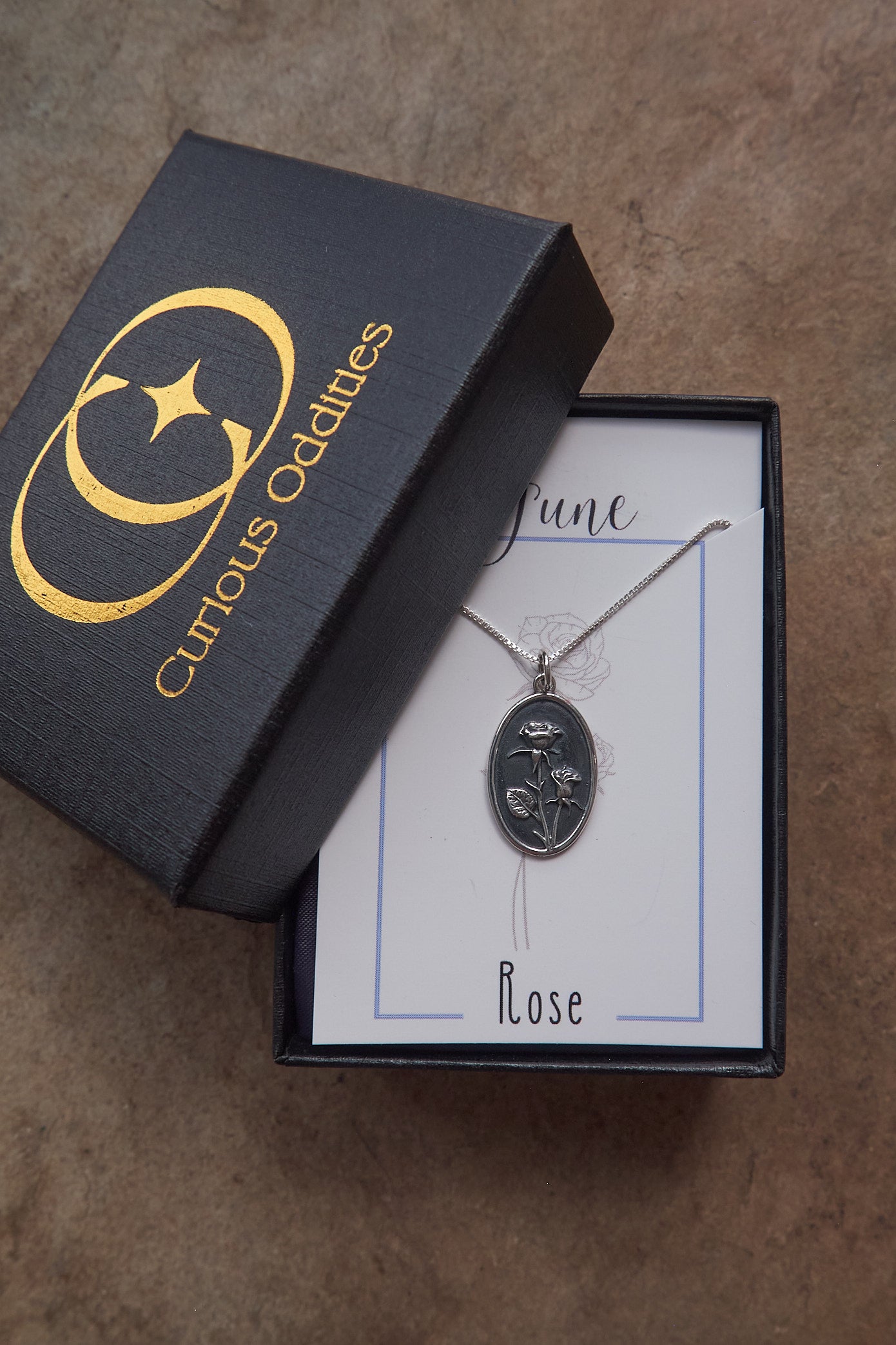 Silver necklace with rose pendant in a 'Curious Oddities' box on a brown surface
