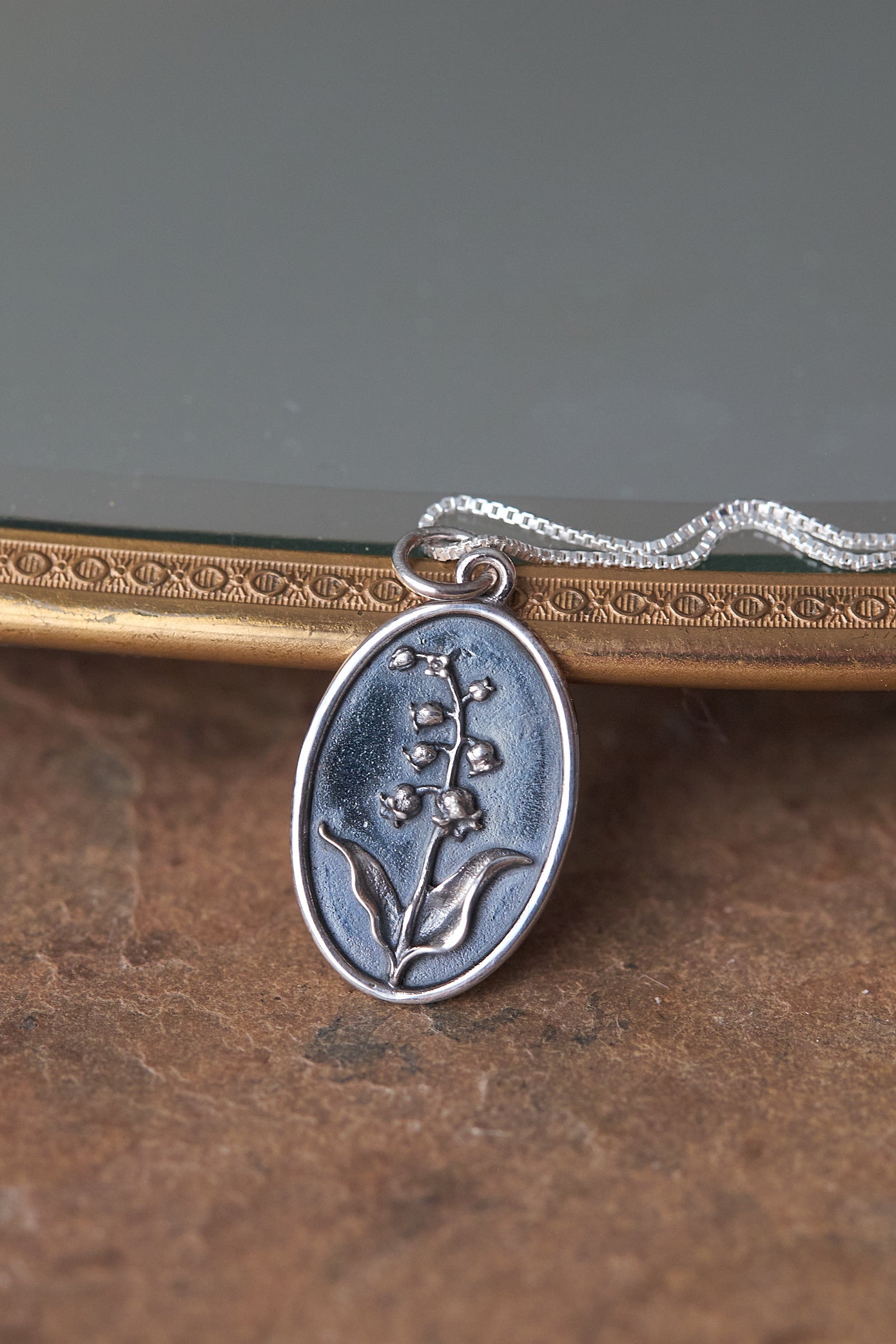 Silver pendant with lily of the valley floral design on a textured surface