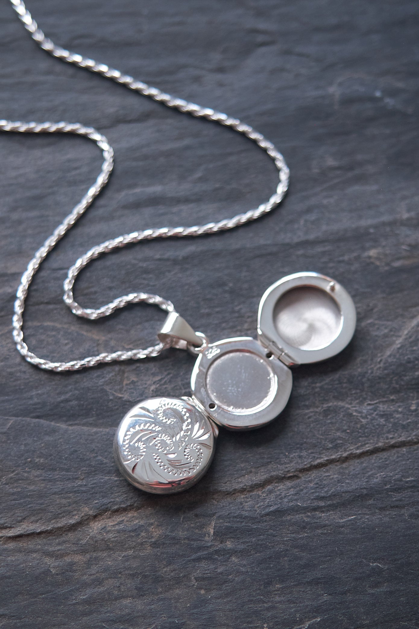 Silver locket necklace shown open on a dark stone surface
