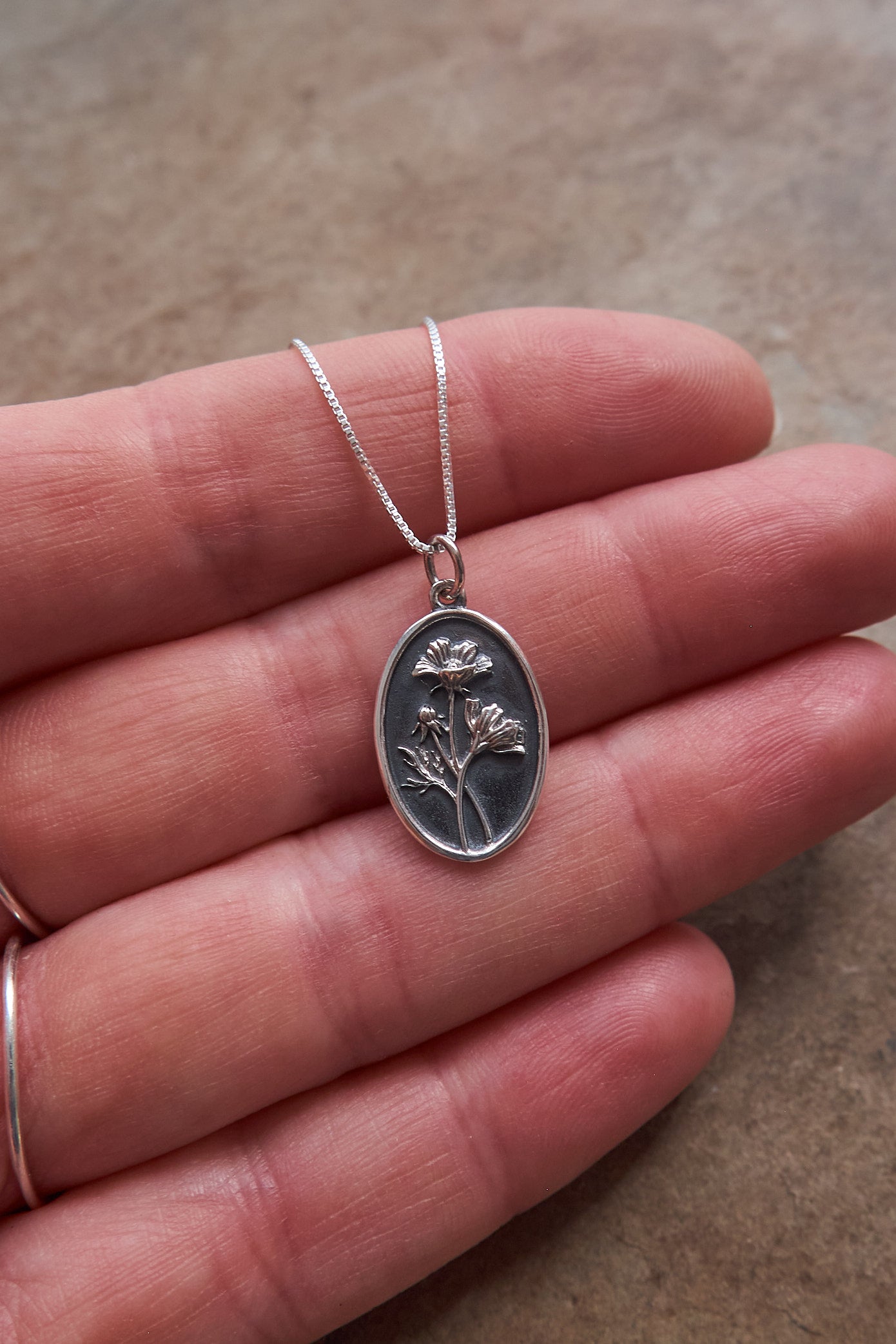 Silver pendant necklace held in a hand against a neutral background