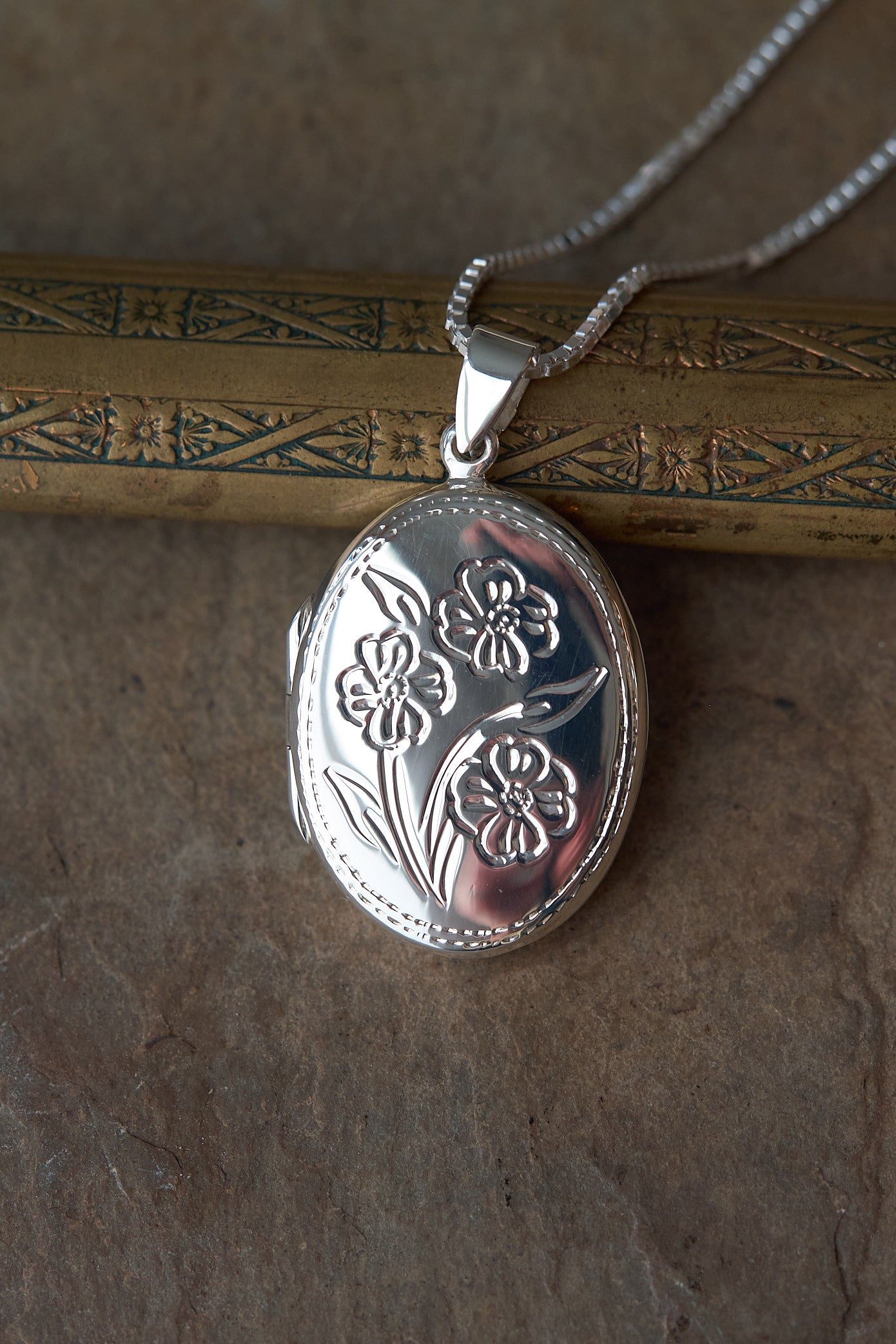 Silver locket with floral design on a textured surface