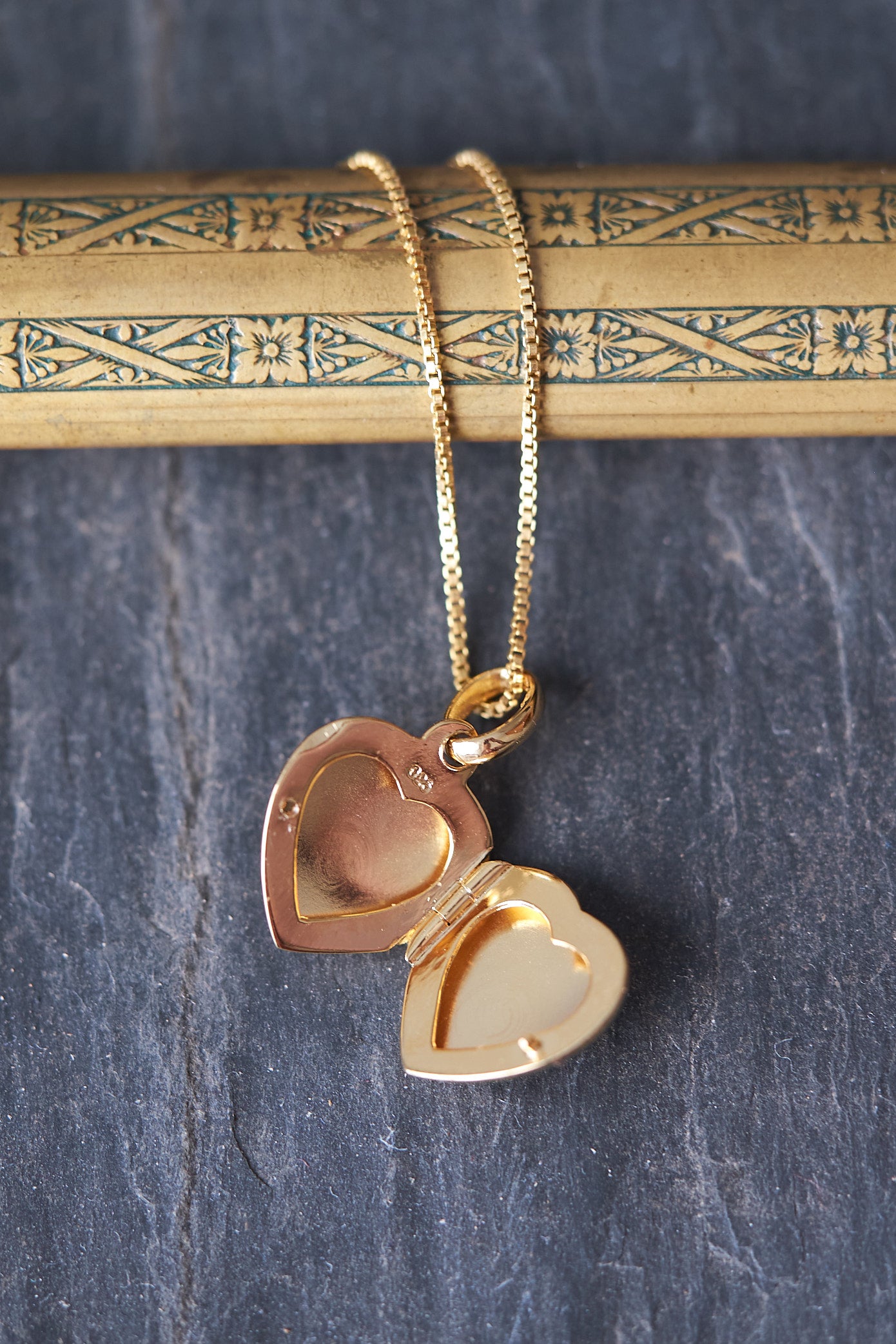 Gold heart-shaped locket necklace shown open on a textured surface
