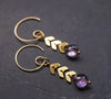 Modern amethyst earrings with gold chevron chain detail on a slate background