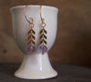 Modern amethyst earrings with gold chevron chain detail displayed in cup
