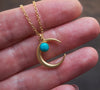 Matte gold half moon necklace with delicate turquoise accent held in hand