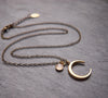 Matte gold half moon necklace with delicate moonstone accent displayed with dark brass chain