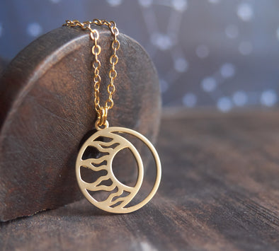 Matte gold moon and sun circle necklace resting on wood spool