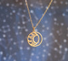 Round, matte gold moon and sun circle necklace in front of blurred celestial background