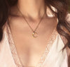 Close up of a gold plated crescent moon necklace with moonstone accent and brass chain worn by dark haired girl with white camisole 