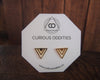 Shiny gold geometric triangle stud earrings displayed on white hexagonal Curious Oddities logo card